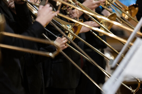 Many people playing the trombone during a performance with their trombone slides being in different positions