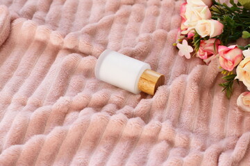 Fototapeta na wymiar Cosmetic crystal bottle on pink blanket with flowers, mockup