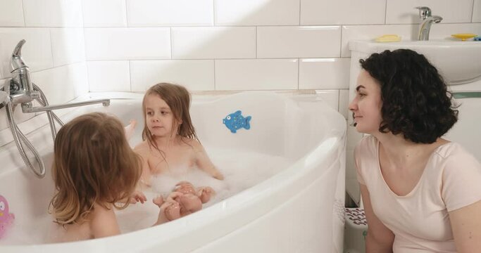 Gender education of twin girls. The mother raises the children during bath procedures.