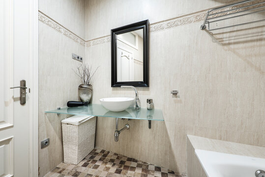 Bathroom with mirror with black wooden frame, white porcelain sink, tempered glass countertop and thick tile floors