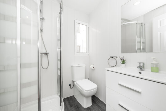White bathroom with frameless wall mirror, white porcelain countertop sink to match wooden drawers and quarter circle shower stall