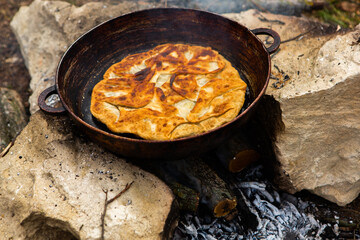 Romanian traditional pie with cheese cooked on a pan on the fire outside. Food from Romania and Republic of Moldova.