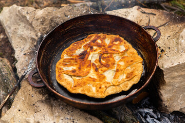 Romanian traditional pie with cheese cooked on a pan on the fire outside. Food from Romania and Republic of Moldova.