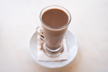 Hot chocolate milk glass on small plate from top. Sweet drink on white table