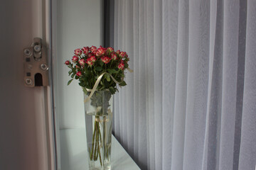 
Bouquet of small pink roses in a transparent glass vase on the windowsill