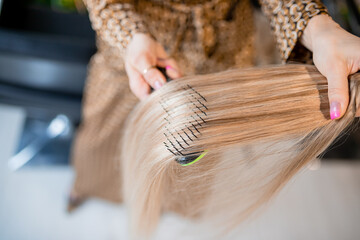 Professional hairdresser prepares blonde hair for extensions and combs them in a beauty salon