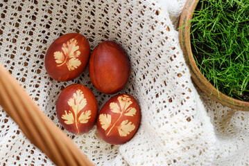 Top view of easter eggs, lying in wicker basket, on a lace doily. Painted brown, with a plant...