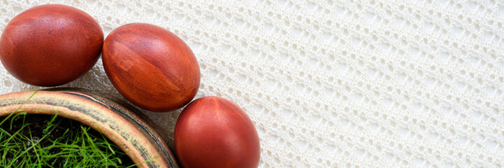 Panoramic photo. Top view of easter eggs, lying on a lace tablecloth. Painted brown. Fresh green oats grass.