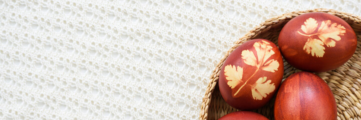 Panoramic photo. Top view of easter eggs, lying in wicker basket, on a lace tablecloth. Painted brown, with a plant theme. Easter concept.