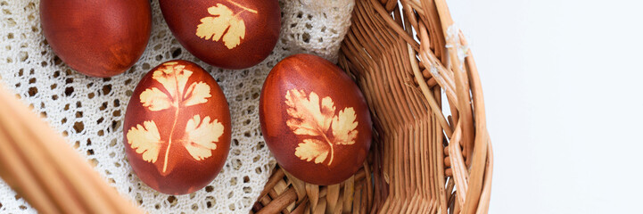 Panoramic photo. Top view od easter eggs, lying in wooden basket, on a lace doily. Painted brown, with a plant motif. Easter basket.