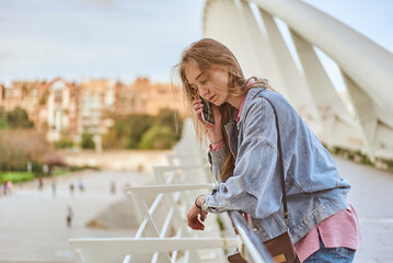 Young white woman talking at her phone on a modern bridge