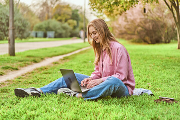young woman working at her laptop while having joy in a beautiful green park