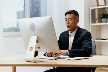 man in a suit sits at a table in front of a computer Lifestyle