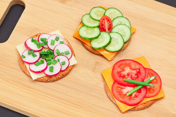 Different Cracker Sandwiches with Tomato, Cucumber, Radish and Cheese on Cutting Board. Easy Breakfast. Diet Food. Quick and Healthy Sandwiches. Crispbread with Tasty Filling. Healthy Dietary Snack