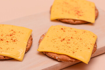 Crispy Cracker Sandwiches with Cheese and Paprika on Wooden Cutting Board and Beige Background