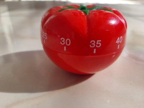 Pomodoro timer in form of a red tomato laying on a wooden table