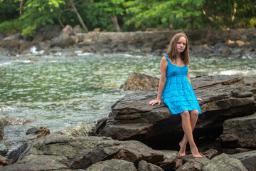 A teenage girl sits on the rocks on a tropical beach.
