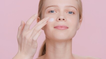 Close-up beauty portrait of young blonde woman applies cream on her face | Smear of cream on woman's face | Skin care product advertising concept.