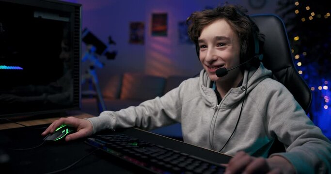 A child addicted to computer games at a young age. College-age boy sits in front of computer at night playing shooters, video game, talking through headset with team members.