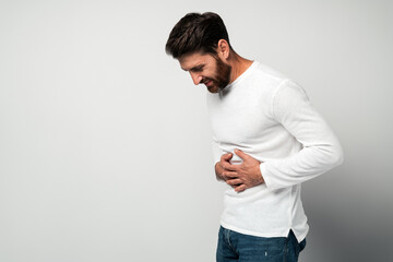 Bearded man standing and holding his painful belly, feeling bad,