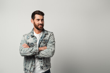 Fototapeta premium Bearded handsome man in casual style looking away and smiling while posing arms crossed