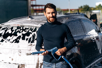 Man washing his car at the street using a high-pressure washer with foam
