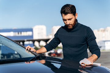 Satisfied concentrated man cleaning the back of his new car while spending time at the street