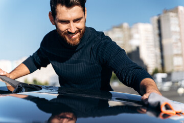 Satisfied concentrated man cleaning the back of his new car while spending time at the street