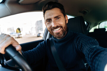 Handsome bearded man holding camera and making selfie while sitting in the car