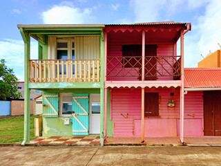 Typical rural Caribbean style houses with pink and green colored walls and headliner, shuttered windows and doors. Tropical architecture and construction. - obrazy, fototapety, plakaty