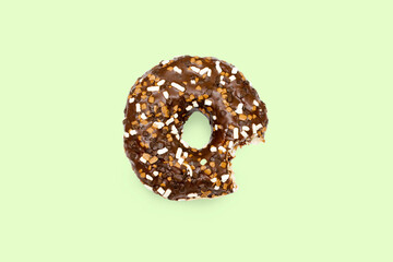 Creative concept of biting eating delicious sweet sugar brown black doughnut donut with glaze on green background. Top view flat lay unhealthy dessert, Food concept, mock up, copy space