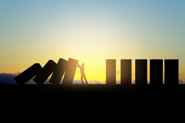 Backlit business man stopping abstract wooden domino blocks on bright sunset sky background with mock up place. Crisis, recession and challenge concept.