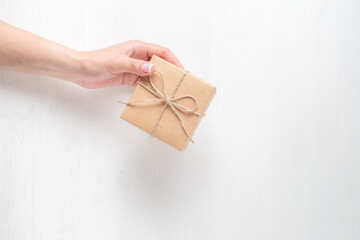 The hand of a young girl holding a gift box. Cardboard box tied with twine. Light background.