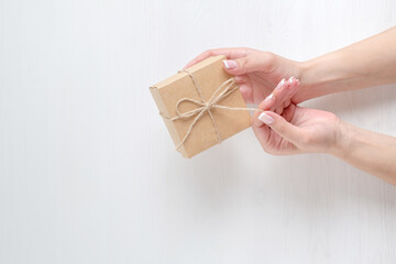 Hands of a young girl holding a gift box. Cardboard box tied with twine. Light back.