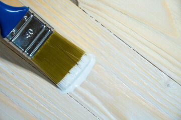 Copy space with paint brush lying on pine wooden background. Close-up paintbrush with liquid white...