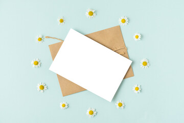 Blank greeting card in frame made of white chamomile or daisy flowers on pastel blue background....