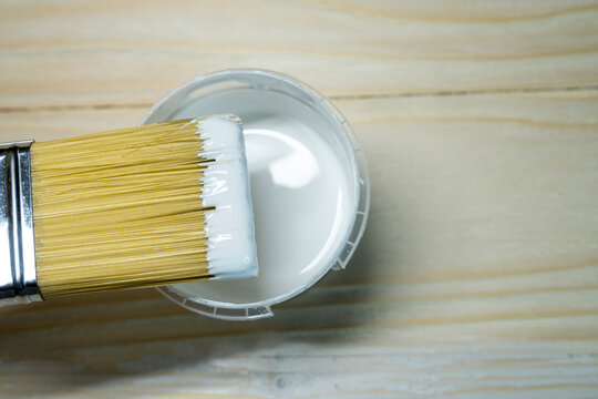 Copy space with paint brush on can lying on wooden background. Close-up paintbrush with liquid white paint on the brush. Painting tools on wooden surface. Top view. Copyspace. Vintage style.