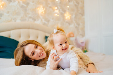 Cute mom and baby daughter lie down, play and hug in bed. games with children. 