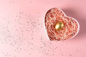 Golden egg in a heart-shaped gift box on a pink background with gold sequins. A Easter egg in gift...