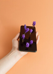 Picture of a woman's hand holding a phone with flowers growing from the screen. Orange background.