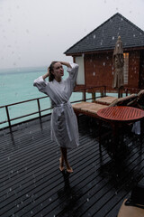 Young girl in white dressing gown under the rain in the Maldives. Bungallow at the background. Island. Rain in the Maldives.