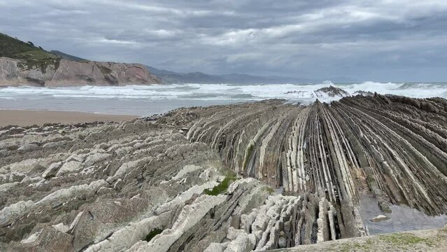 Rough sea waves breaking on sharp limestone rock layers in Zumaia beach on cloudy day. Popular flysch landmark in the Basque Country