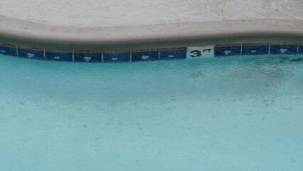Rain drops falling on water surface of blue swimming pool, rainy day in motel or hotel, California USA. Rainfall on summer vacations, raindrops splashing during monsoon. Seamless looped cinemagraph.