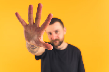 Caucasian bearded tattooed guy stretching his hand to the camera and trying to cover it with his...