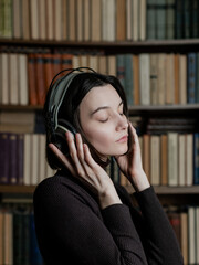Woman in headphones listening to audiobooks on background of library shelves with paper books