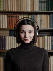 Woman in headphones listening to audiobooks on background of library shelves with paper books