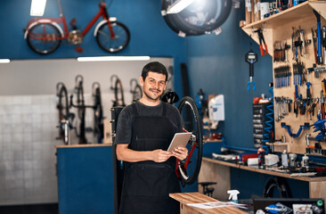 Technology has its place, even in bicycle repair. Shot of a man using a digital tablet in a bicycle repair shop.