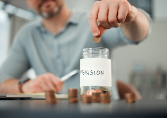 Its important to save. Cropped shot of an unrecognizable man putting coins into a jar marked PENSION while working on his finances at a desk at home.