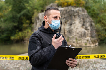 One man police detective or inspector securing crime scene using radio for communication waiting for back up during investigating procedure collecting evidence near the river in day nature copy space