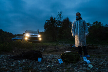 Forensic police investigator collecting evidence at the crime scene in nature at night murder...